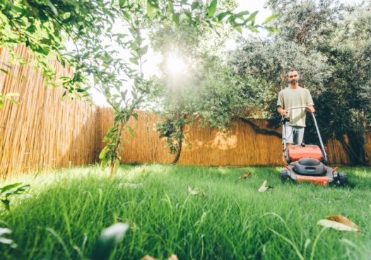 Un homme est en train de tondre la pelouse de son jardin à l’aide d’une tondeuse manuelle.