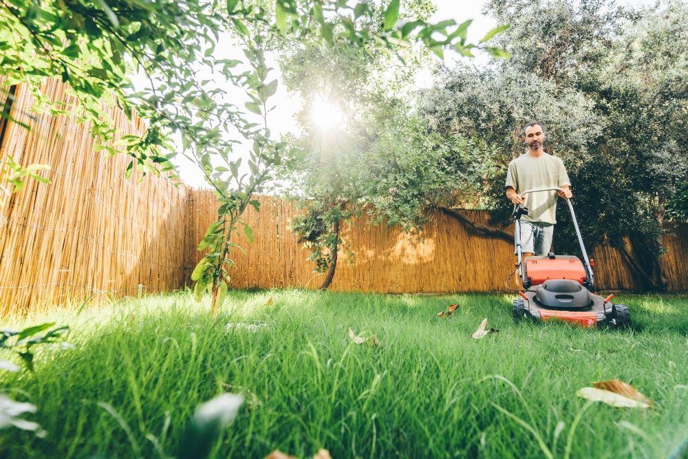 Un homme est en train de tondre la pelouse de son jardin à l’aide d’une tondeuse manuelle.