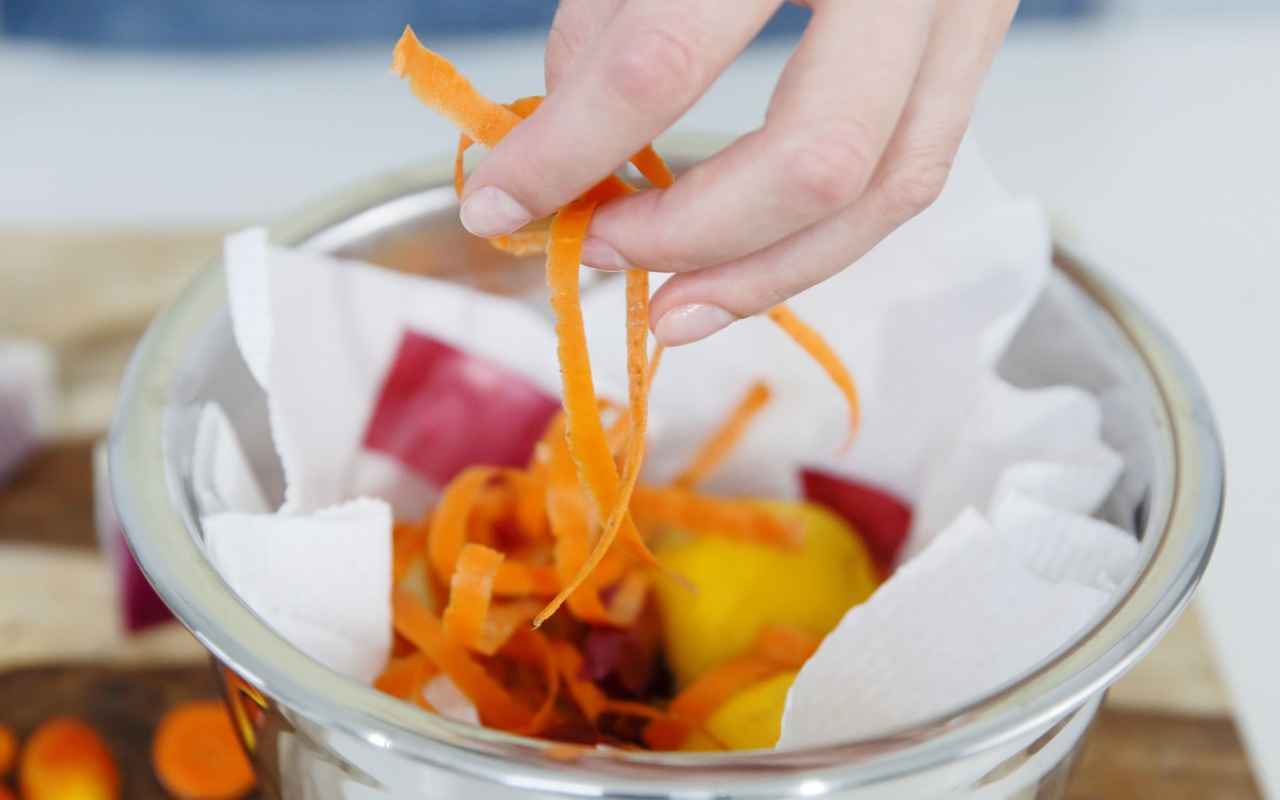 Main qui dépose des épluchures de carottes dans un bol en verre contenant d'autres épluchures pour le compost